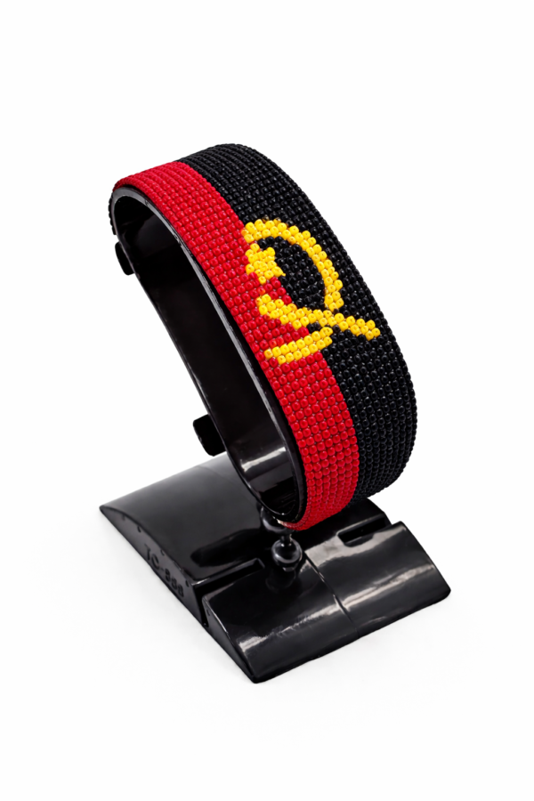 Handcrafted Angola flag bracelet made with red, black, and yellow beads, adjustable beaded wrist accessory, displayed on a black stand.