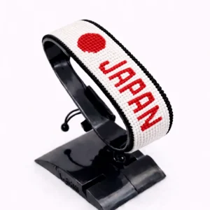 Handcrafted Japan name flag bracelet with red and white beads and customizable name, adjustable beaded wrist accessory, displayed on a black stand.