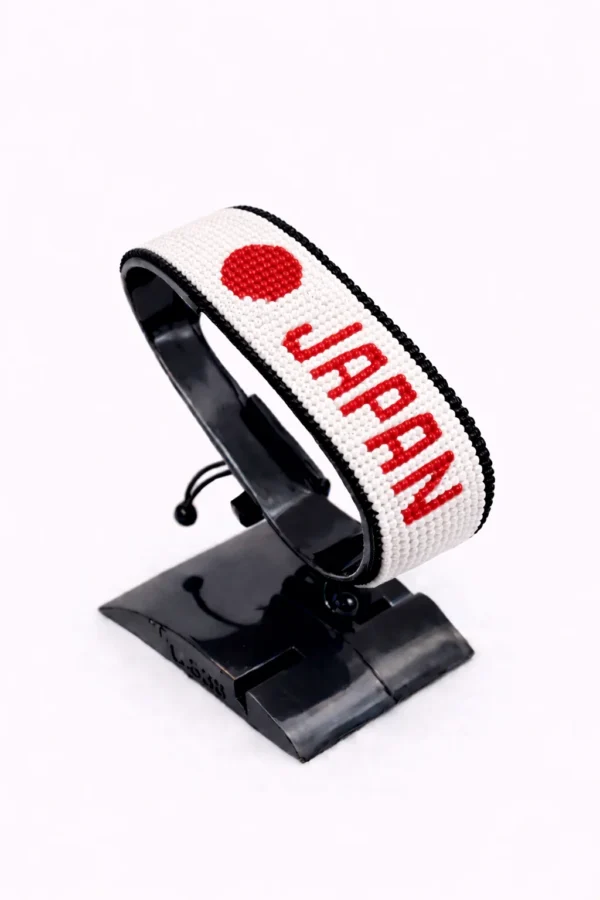 Handcrafted Japan name flag bracelet with red and white beads and customizable name, adjustable beaded wrist accessory, displayed on a black stand.