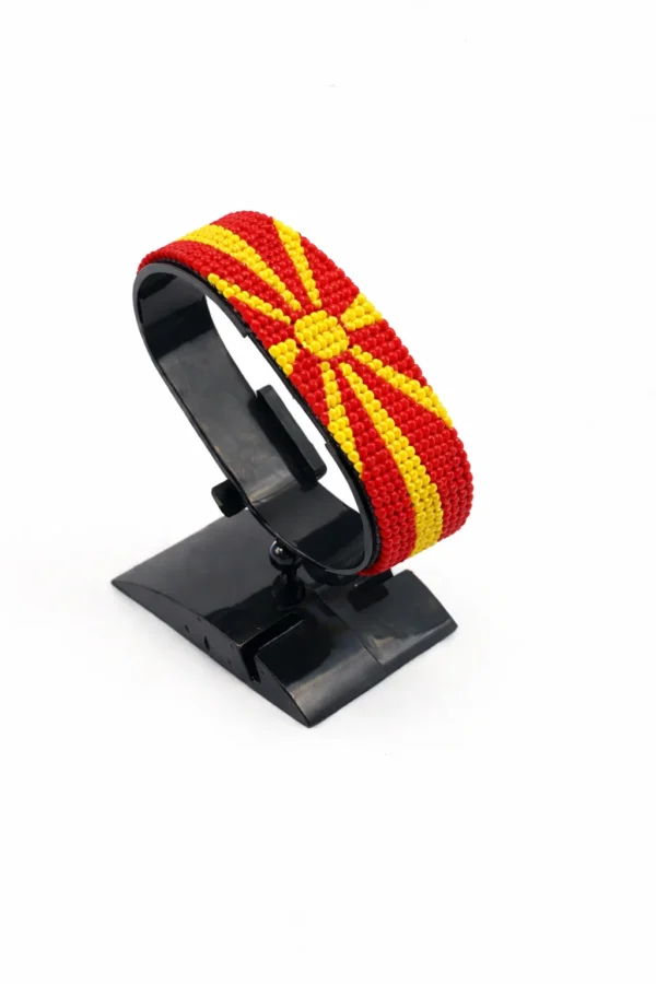Handcrafted North Macedonia flag bracelet made with red and white beads, adjustable beaded wrist accessory, displayed on a black stand
