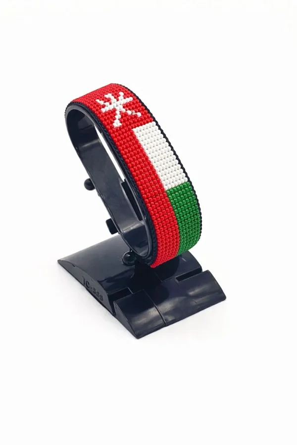 Handcrafted Oman flag bracelet made with red and white beads, adjustable beaded wrist accessory, displayed on a black stand