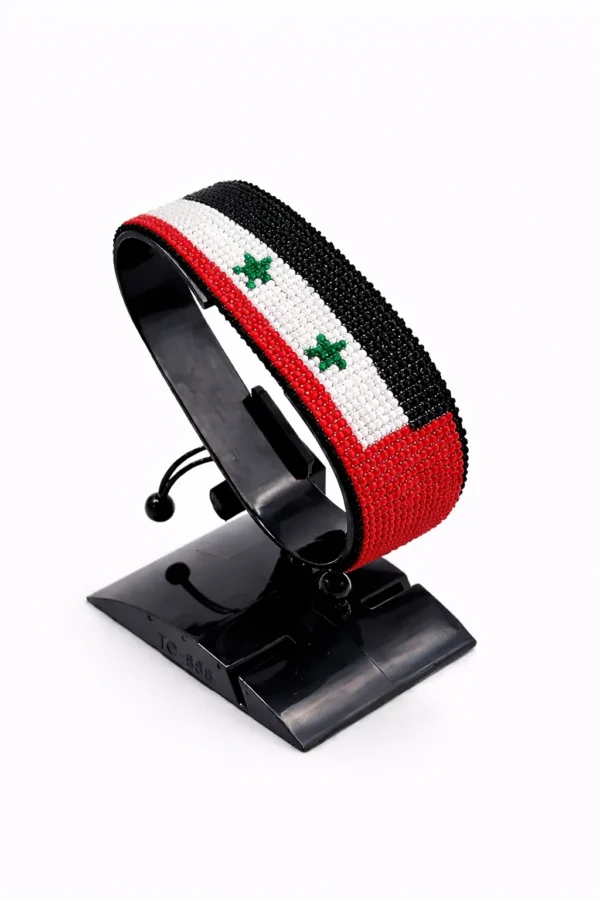 Handcrafted Syria flag bracelet made with red and white beads, adjustable beaded wrist accessory, displayed on a black stand