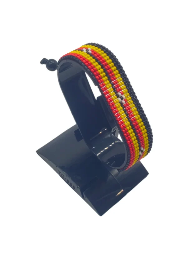 Handcrafted Uganda flag bracelet made with red and white beads, adjustable beaded wrist accessory, displayed on a black stand