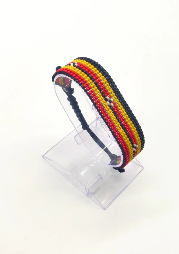 Handcrafted Uganda flag bracelet made with red and white beads, adjustable beaded wrist accessory, displayed on a Clear stand