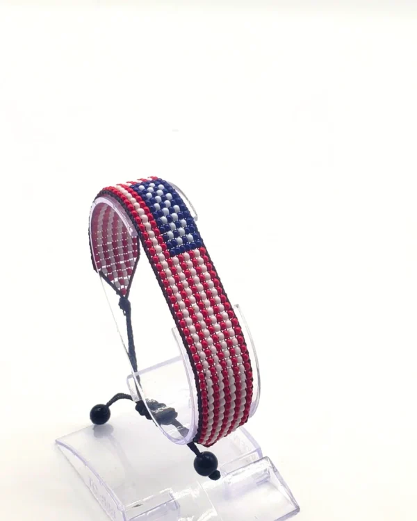 Handcrafted USA flag bracelet made with red and white beads, adjustable beaded wrist accessory, displayed on a black stand.