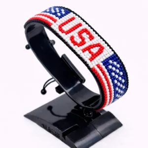 Handcrafted USA flag bracelet made with red and white beads, adjustable beaded wrist accessory, displayed on a black stand.